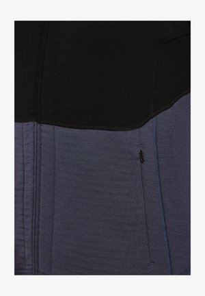 Farbblockiertes Sportoberteil mit schwarzem oberen Abschnitt und dunkelblauem unteren Abschnitt. Verfügt über einen strukturierten Stoff und eine seitliche Reißverschlusstasche.