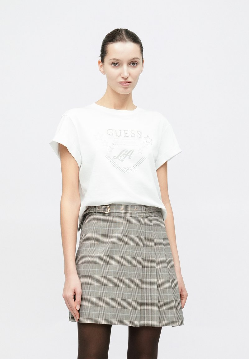 Wit katoenen T-shirt met opgerolde mouwen en een zilveren grafische print; grijze geruite geplooide rok met riemlussen en twee voorzakken.