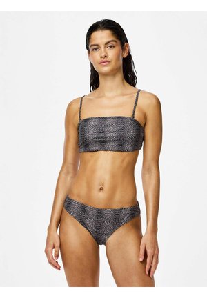 Mladá žena so mokrými vlasmi, ktorá má na sebe dvojdielne plavky s leopardím vzorom na jednoduchom bielom pozadí.