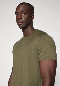 Olive green short-sleeve t-shirt in soft, textured fabric with a crew neckline and clean stitching, viewed from the left side against a light background.