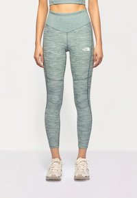 Leggings a vita alta in un tessuto ceruleo testurizzato con un dettaglio del logo sulla coscia sinistra. Abbinati a scarpe da ginnastica nei toni neutri.