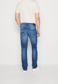 Vaqueros de denim azul ajustados con una etiqueta de cuero marrón en la parte trasera de la cintura, que cuentan con dos bolsillos traseros y una textura desteñida.