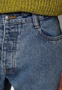 Světle modré džíny z denimu s bledým vzorem, měděným prošíváním, kovovým zapínáním na knoflík a hnědou koženou nášivkou na zadním pásku.