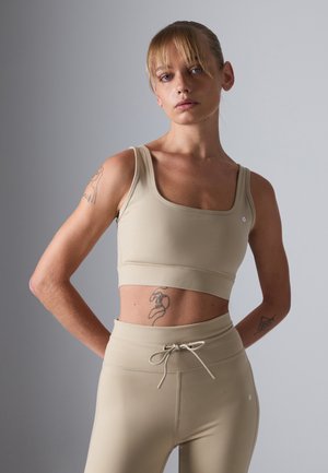 Beige Activewear-Set bestehend aus einem taillierten Crop-Top mit quadratischem Ausschnitt und hochgeschnittenen Leggings mit Kordelzug, glatter Textur.