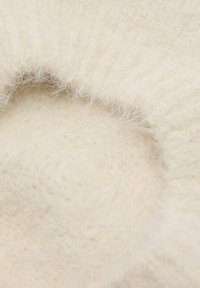 Tessuto color crema con una superficie morbida e pelosa, caratterizzato da una forma circolare e delicate creste nel motivo della tessitura.