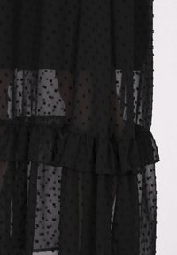 Schwarzes, transparentes Kleid mit gepunktetem Muster, gerafftem Saum und leichtem Stoff, der ein geschichtetes, fließendes Design bietet.
