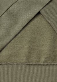 Tela verde oliva con una textura suave, que presenta un dobladillo acanalado y secciones superpuestas, creando profundidad en el diseño.