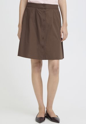 Brun knælængde nederdel med knapper foran, båret med mørke spidse flade sko, vist fra talje til fødder mod en ensfarvet baggrund.