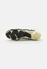 Suela de zapatilla deportiva en negro y crema con un patrón texturizado, múltiples tacos para tracción y un diseño aerodinámico elegante.