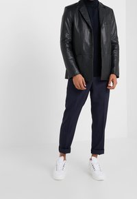 Černé kožené sako s přizpůsobeným střihem, jednořadým zapínáním a klopovými límci. Nosené přes námořnický rolák, v kombinaci s námořnickými kalhotami a bílými teniskami.