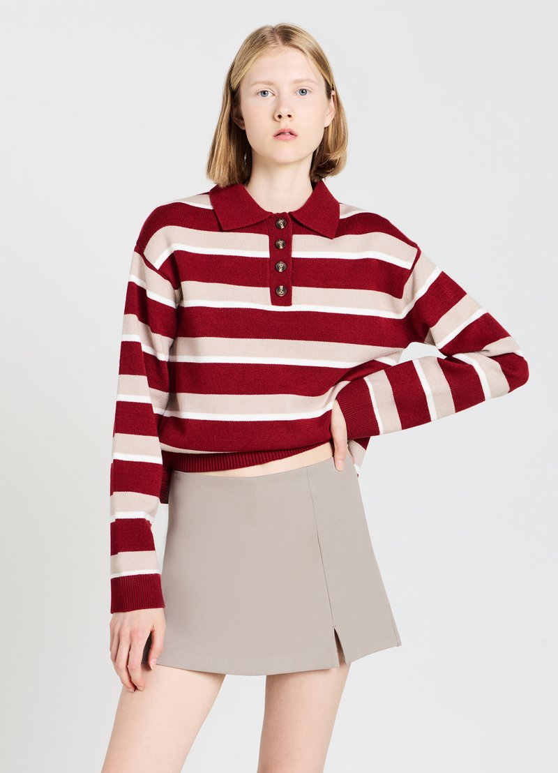 Gestreifter Pullover in Rot und Beige mit Kragen und vier Knöpfen, kombiniert mit einem hellbeigen Minirock mit einem Schlitz vorne.