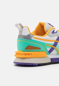 Sneaker multicolore con parte superiore bianca, accenti turchesi, fodera arancione e dettagli viola. Include una suola testurizzata e ventole laterali in rete.