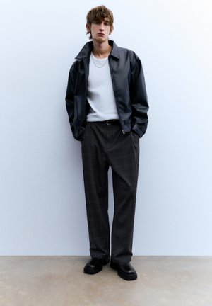 Svart läderjacka, vit t-shirt med rund hals, grå rutiga byxor, svart bälte och kraftiga svarta skor, mot en enkel bakgrund.