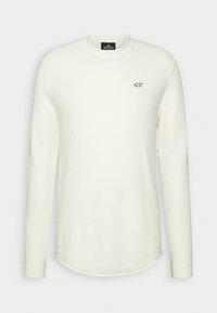 Pull en maille blanc à manches longues avec col rond, tissu texturé, petit logo mouette noir sur le côté gauche de la poitrine, et ourlet arrondi.