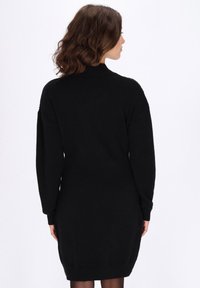 Zwart gebreid jurk met een hoge halslijn, lange mouwen en geribbelde zoom. Zachte textuur met een aansluitende silhouet, minimalistisch ontwerp.