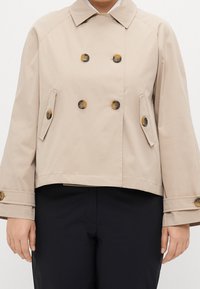Beige kort peacoat med dubbelknäppt design, stora bruna knappar, två sidfickor och knäppta ärmslut. Slät, hållbar tyg.