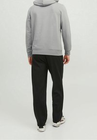 Sudadera con capucha gris y corte relajado, combinada con pantalones jogger negros. Textura suave y diseño sencillo, acompañada de zapatillas deportivas con un diseño estampado.