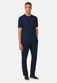 Námořnické modré bavlněné tričko s kulatým výstřihem v kombinaci s ladícími kalhotami, které mají volný střih a minimalistický design. Celý outfit doplňují černé tenisky.