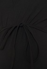 Tissu noir avec un cordon de serrage centré qui crée des plis froncés autour de la taille.