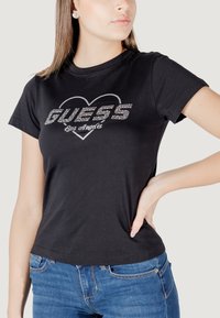 Zwarte T-shirt van katoen, met een strasstenen 'GUESS' logo en de tekst 'Los Angeles' in een hartontwerp. Korte mouwen, ronde hals.