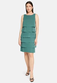 Robe à couches bleu sarcelle avec un design sans manches, comportant trois volants horizontaux. Le tissu semble léger, avec une texture lisse.