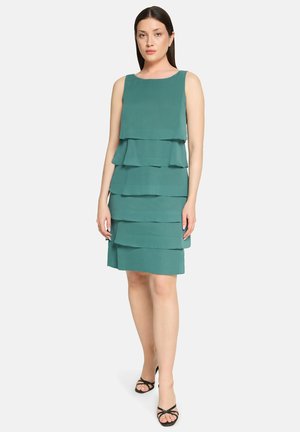 Morska zielona sukienka warstwowa bez rękawów, z trzema poziomymi falbanami. Tkanina wydaje się lekka, o gładkiej fakturze.