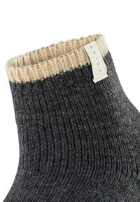 Gray knitted sock with a ribbed texture, featuring a beige cuff and a small fabric tag. Distinct color contrast at the ankle area.