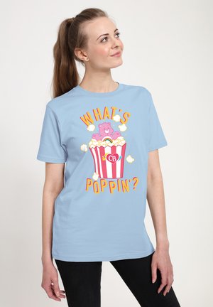 Lyseblå kortærmet T-shirt med et farverigt grafisk motiv af en bjørn i en popcornspand og teksten "HVAD'S POP" i orange og gul.