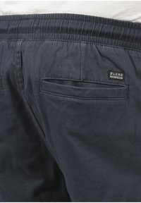 Shorts en tissu tissé bleu foncé avec une taille élastique, deux poches arrière et une petite étiquette de marque "BLEND" sur la poche droite.