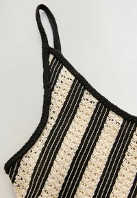 Virkat topp med svarta och gräddfärgade ränder, dekorativa öppna mönster och en flätad svart rem. Texturerat material med en lätt och luftig design.
