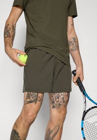 Olijfgroene sportshorts en bijpassend T-shirt, met een gladde stof, een ontspannen pasvorm en zijzakken, vergezeld van een tennisbal en racket.