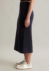 Strickmidirock in Marineblau mit strukturiertem Muster. Getragen mit weißen und beigen Turnschuhen, verfügt er über eine taillierte Taille und einen ausgestellten Saum.