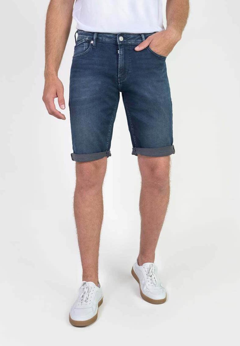 Pantalones cortos de mezclilla, azul oscuro, con un ajuste relajado y dobladillos enrollados. Equipados con bolsillos delanteros y traseros. Combinados con zapatillas blancas.