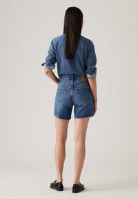 Camisa de denim, mangas largas enrolladas, combinada con pantalones cortos de denim de cintura alta. Lavado en azul claro, con dobladillo deshilachado y bolsillos traseros con el logotipo de la marca.