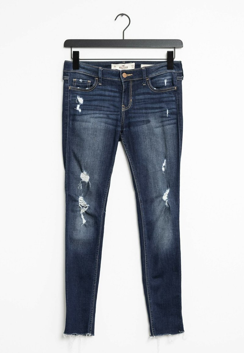 Mörkblå denim skinny jeans med slitna partier och fransad fåll, med en klassisk femfickdesign och knappstängning.