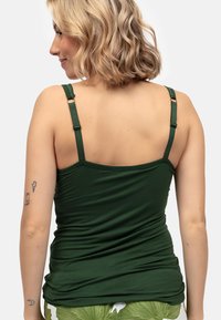 Ciemnozielony top na ramiączkach z regulowanymi paskami i marszczonym wzorem. Widok z tyłu ukazuje gładką teksturę i dopasowany krój.