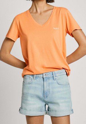 Pomarańczowy t-shirt z dekoltem w serek, wykonany z miękkiego materiału, z krótkimi rękawami. W zestawie z jasnoniebieskimi szortami dżinsowymi, lekko spranymi z podwiniętymi mankietami.