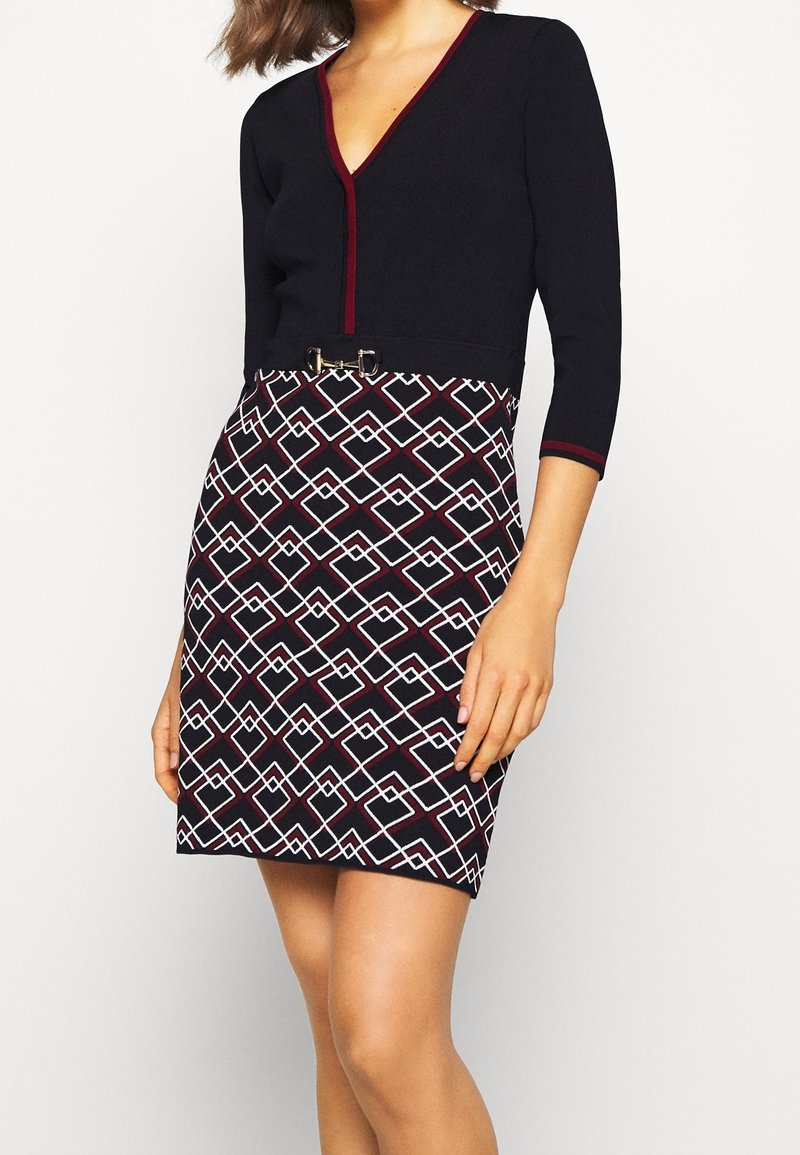 Robe noire et bordeaux avec manches trois-quarts, col en V et motif géométrique blanc et bordeaux sur la jupe avec une petite ceinture décorative.