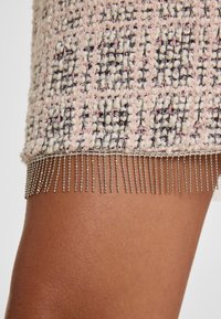 Knie-lange tweed rok in lichtroze en zwart met een textuurpatroon en metallic franjes aan de onderkant.