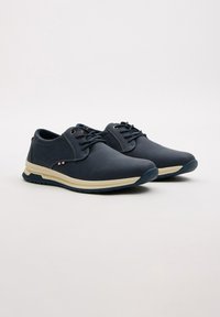 Zapatos azul marino con una parte superior sintética suave, una entresuela de un beige claro y una suela de goma negra, con punta redondeada y cierre de cordones.