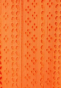 Pomarańczowy haftowany materiał z misternymi wzorami kwiatowymi i pętlami, o gładkiej teksturze i jednolitym detalu ściegów na całej powierzchni.