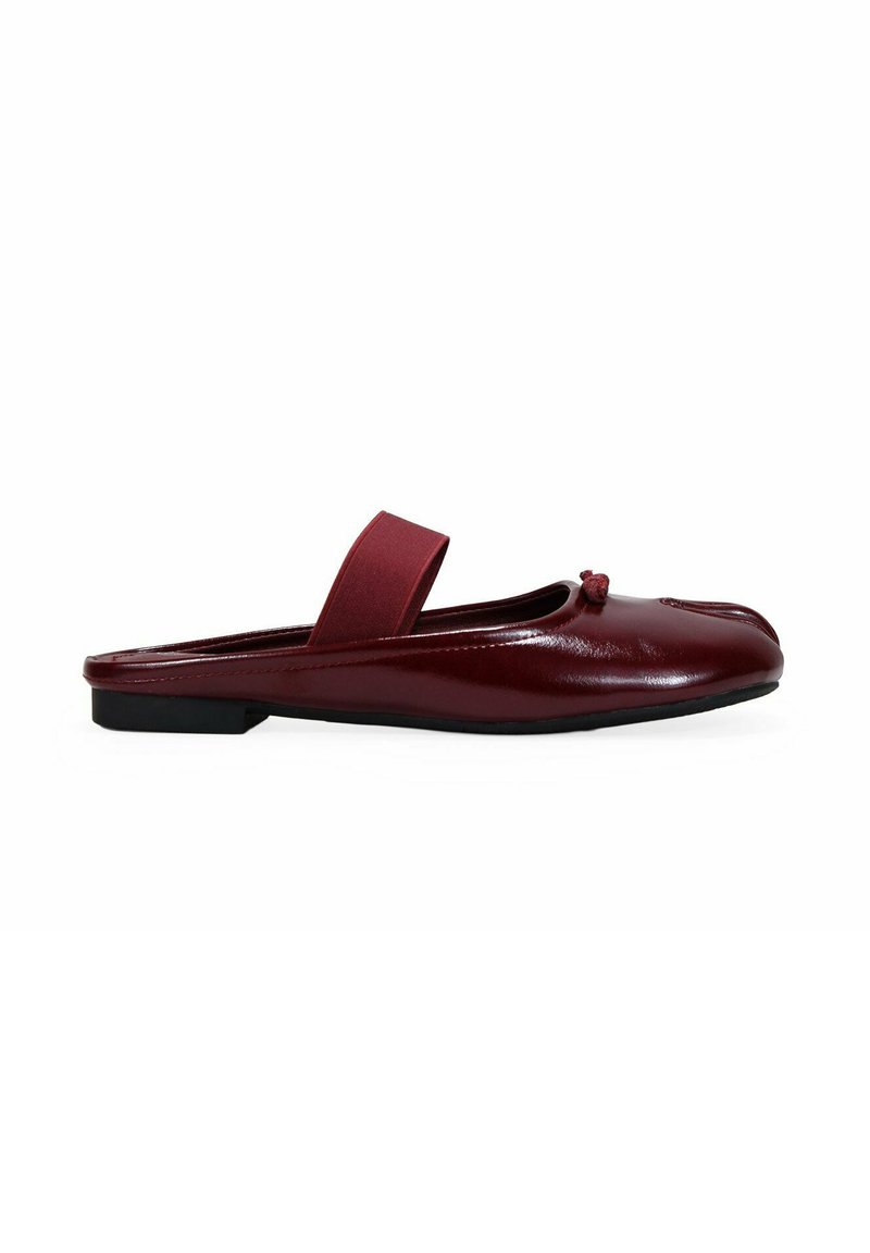 Zapato burdeos tipo slip-on con un acabado de cuero suave, punta redonda, tira elástica y un pequeño detalle de nudo en la parte delantera. Suela plana.