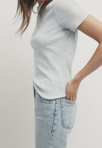 Lysegrå ribbet kortærmet top parret med lyseblå højtaljede jeans, der fremhæver en tætsiddende design og subtile teksturdetailler.
