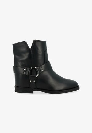 Bottes noires à la cheville en cuir lisse. Présente une découpe en V sur le haut, une sangle avec une boucle ronde, et un petit talon.