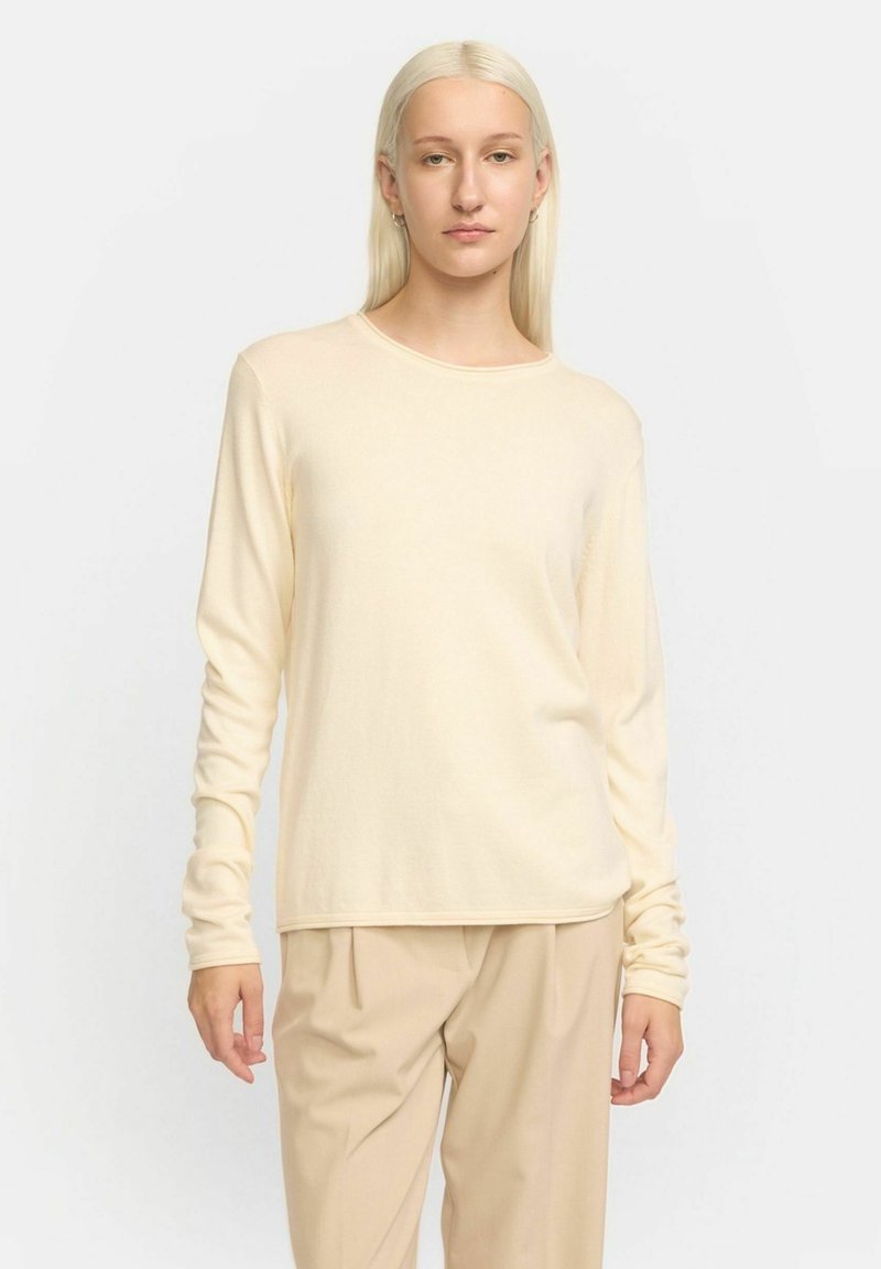 Crème langemouwen top van een zachte, lichte stof met een ronde hals en een ontspannen pasvorm, gecombineerd met beige broeken.