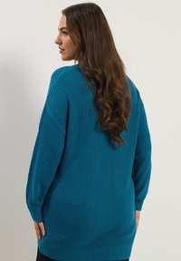 Turkusowy sweter dzianinowy o luźnym kroju, z długimi rękawami, prążkowaną teksturą i okrągłym dekoltem. Miękki materiał opada do bioder.