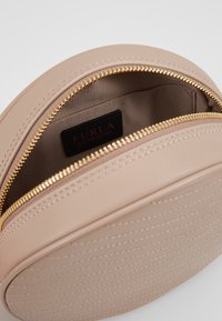 Runde Handtasche aus weichem beigefarbigen Leder mit strukturiertem Boden. Verfügt über einen goldenen Reißverschluss und ein gefüttertes Innenleben, das ein Markenlabel zeigt.