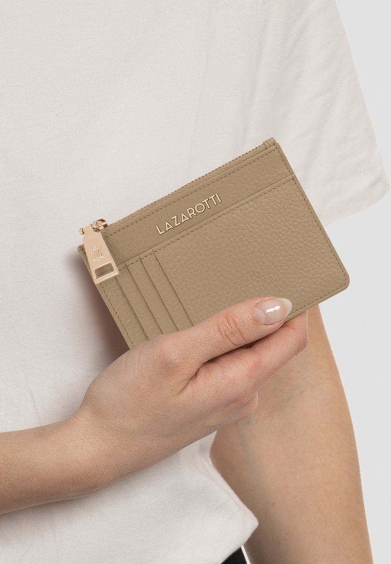 Portafoglio beige con texture e dettagli in oro, dotato di scomparti per carte e di un compartimento con zip, tenuto in mano contro una camicia bianca.