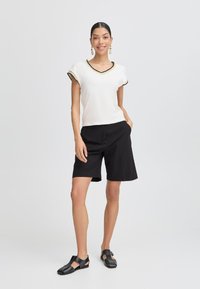 Top bianco a maniche corte con scollo a V e rifiniture nere, abbinato a pantaloni corti neri di media lunghezza e sandali neri. Tessuto morbido, design informale.