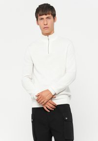 White zip-neck sweater with long sleeves, ribbed cuffs and hem, soft texture, paired with black cargo pants featuring side pockets.